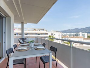 A balcony with a table set for four, chairs, and a view of the cityscape and mountains. - Port Canigó by Interhome (Roses)