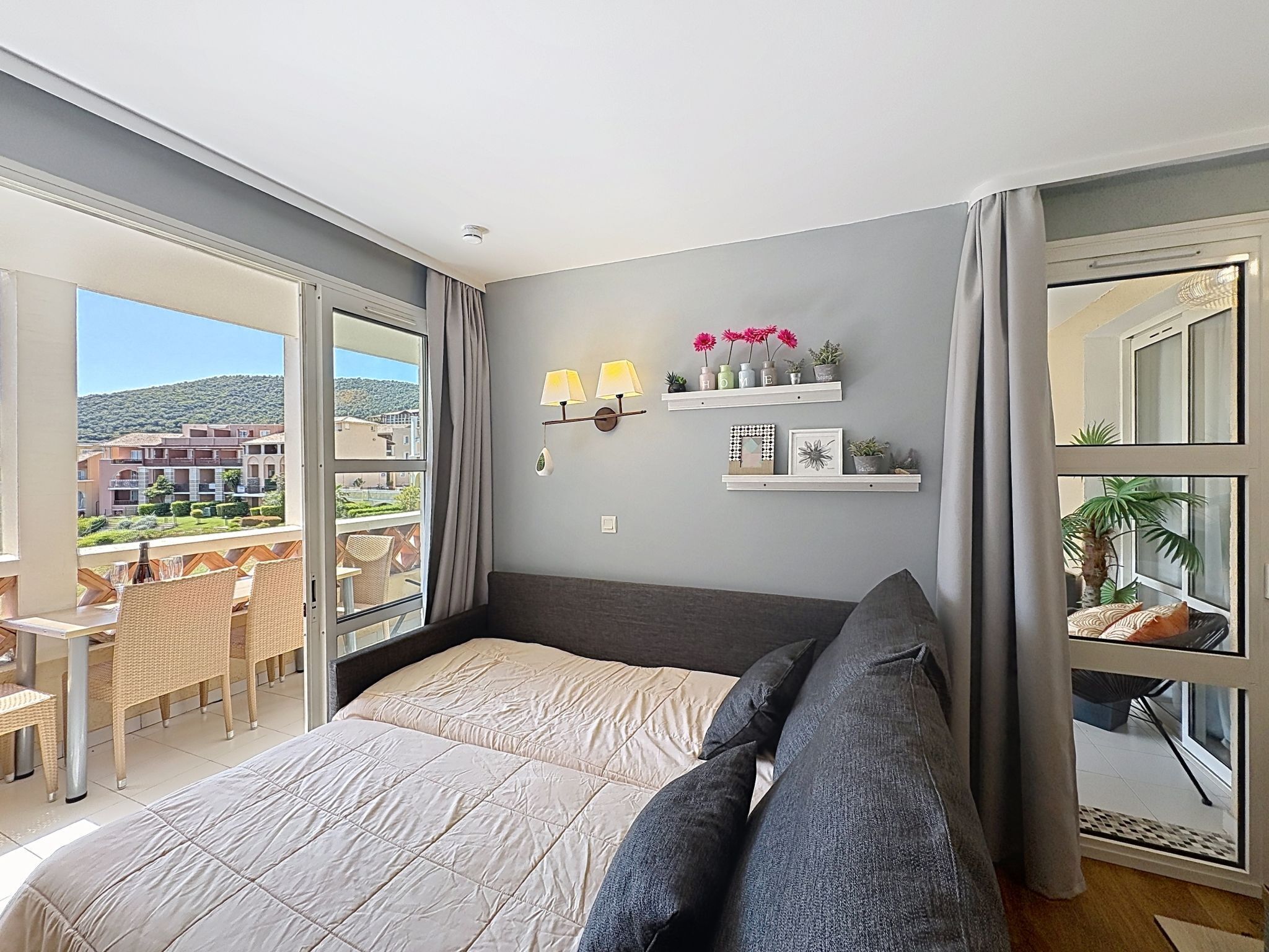 A bedroom with a bed, a balcony, a dining area, and a view of buildings.