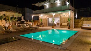 Ein Außenpool bei Nacht mit Liegestühlen, einer überdachten Lounge und Topfpflanzen.