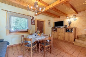 Un comedor con una mesa dispuesta para cuatro, sillas de madera, una lámpara de araña y un ventanal con vistas a árboles.