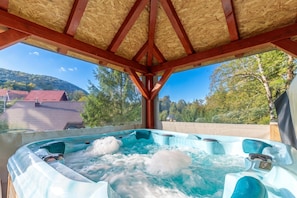 A hot tub with a wooden roof structure and a view of a residential area and trees.