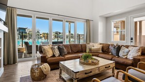 Uma sala de estar espaçosa com sofá de couro, mesa de centro de madeira e vista para uma piscina através de grandes portas de vidro.
