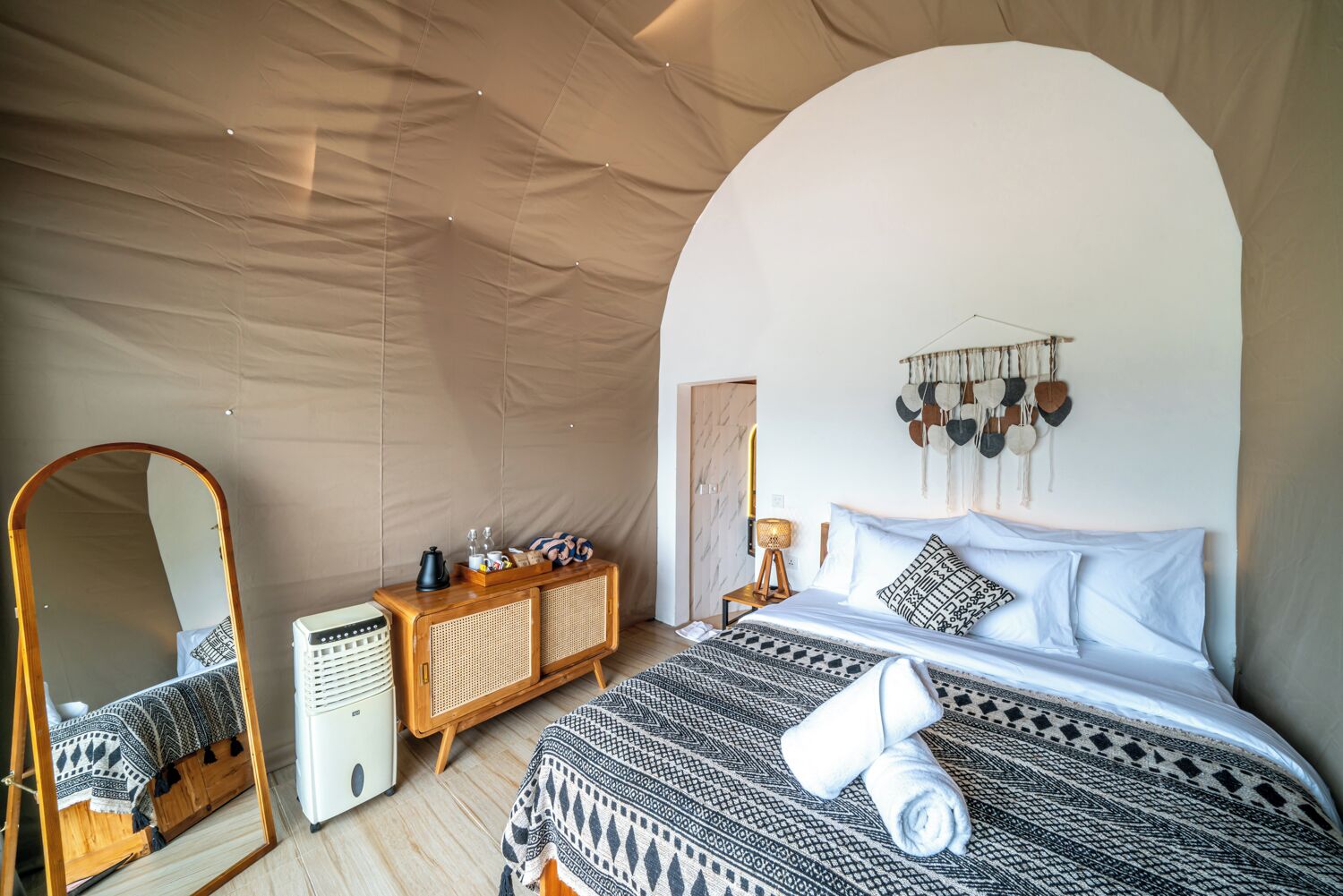 Ein Zeltraum mit einem Bett, einem Schminktisch, einem Spiegel und einer Wand mit hängenden Gegenständen.