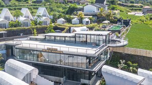 A modern hotel with a glass facade, named 'The Giri Resto The Dewi Kintamani.' It features a rooftop terrace with seating and a pool. - The Dewi Kintamani (Kintamani)