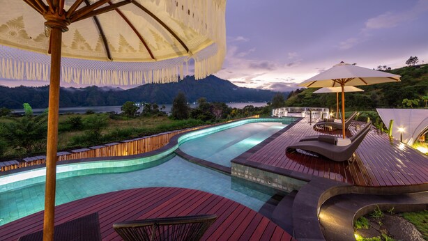 A swimming pool with a wooden deck, lounge chairs, and umbrellas. - The Dewi Kintamani (Kintamani)
