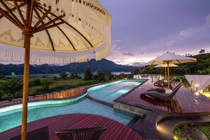 A swimming pool with a wooden deck, lounge chairs, and umbrellas. - The Dewi Kintamani (Kintamani)