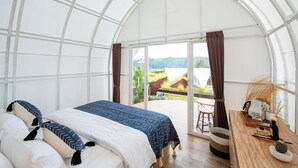 A spacious room with a large bed, a wooden desk, and a view of a garden through a glass ceiling. - The Dewi Kintamani (Kintamani)