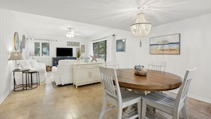 Un vaste espace de vie comprenant une table à manger en bois, des meubles blancs et un lustre.