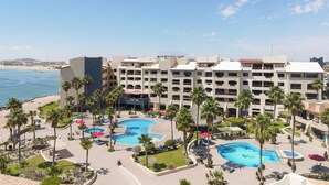 Een resort met meerdere zwembaden, palmbomen en uitzicht op het strand.