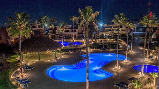 Een nachtzicht van een resort met meerdere zwembaden, palmbomen en loungeruimtes.
