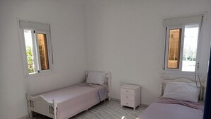 Un dormitorio con dos camas individuales, una mesita de noche y una ventana.