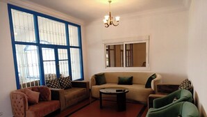 Una sala de estar con sofá, sillones, una mesa de centro y un ventanal con marcos azules.