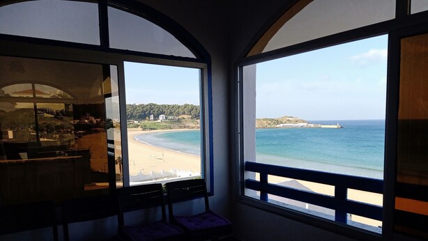 Una habitación con ventanas amplias que dan a una playa y un paisaje montañoso.
