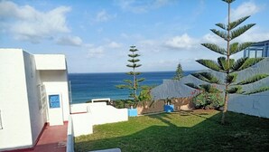 Vista de una propiedad costera con un edificio blanco, un pequeño jardín y vistas al océano.