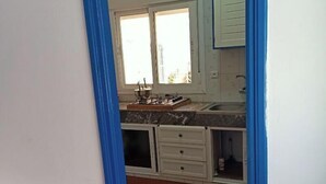 Una cocina con armarios blancos, un ventanal y piso de baldosas.