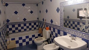 A bathroom with a checkered floor, a bathtub, a toilet, and a bidet.