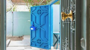 Un cancello blu con un motivo geometrico, un pavimento a scacchi e una porta in metallo con maniglia in ottone.