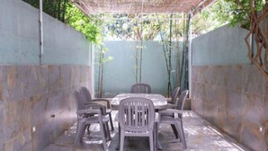 Un espace extérieur abrité, aménagé avec une table et des chaises, entouré de murs en pierre et de plantes en bambou.