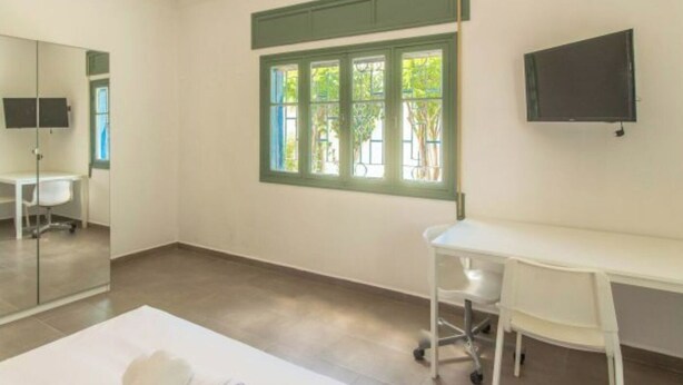 Une chambre d’hôtel avec un lit, un bureau, une chaise, une télévision et une fenêtre avec des volets verts.