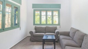Un salon avec un canapé beige, une petite table et une fenêtre avec des volets verts.