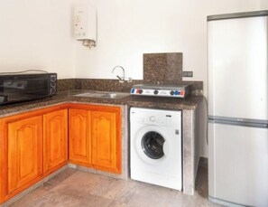 A compact kitchen with wooden cabinets, a washing machine, a microwave, and a refrigerator.