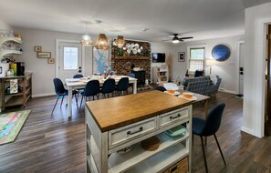 A dining area with a wooden table, chairs, and a brick wall. There is a television on the wall and a bookshelf with books and decorative items. - Welcome to Kingfisher Cabin! (MOORESVILLE)
