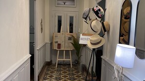 En hall med mönstrade golvplattor, en kristallkrona, ett bord med en lampa och en utställning av hattar.
