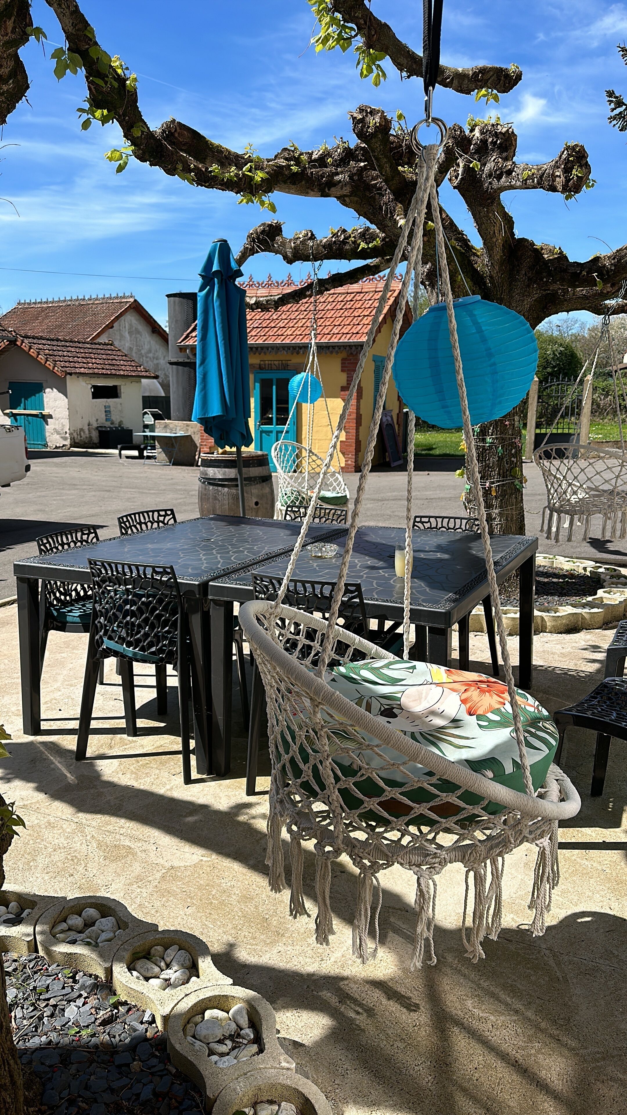 Terras met tafels en stoelen, een hangmat en een gebouw met pannendak op de achtergrond.
