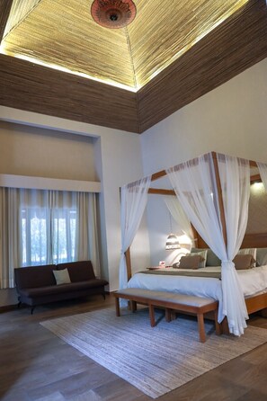 A bedroom with a four-poster bed, a sofa, and a large window with curtains.