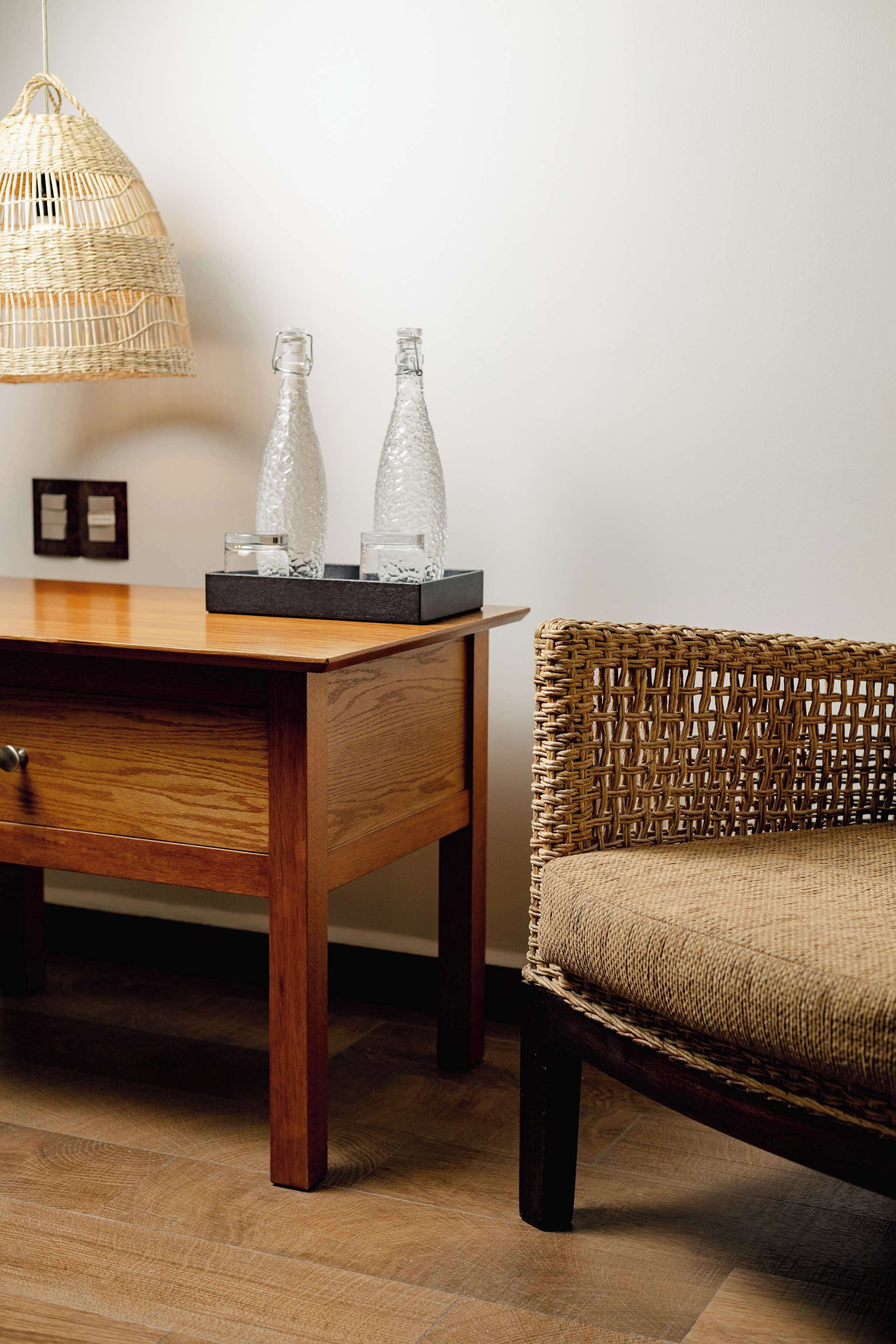 A wicker chair, a wooden table with a tray, and a hanging wicker lamp.