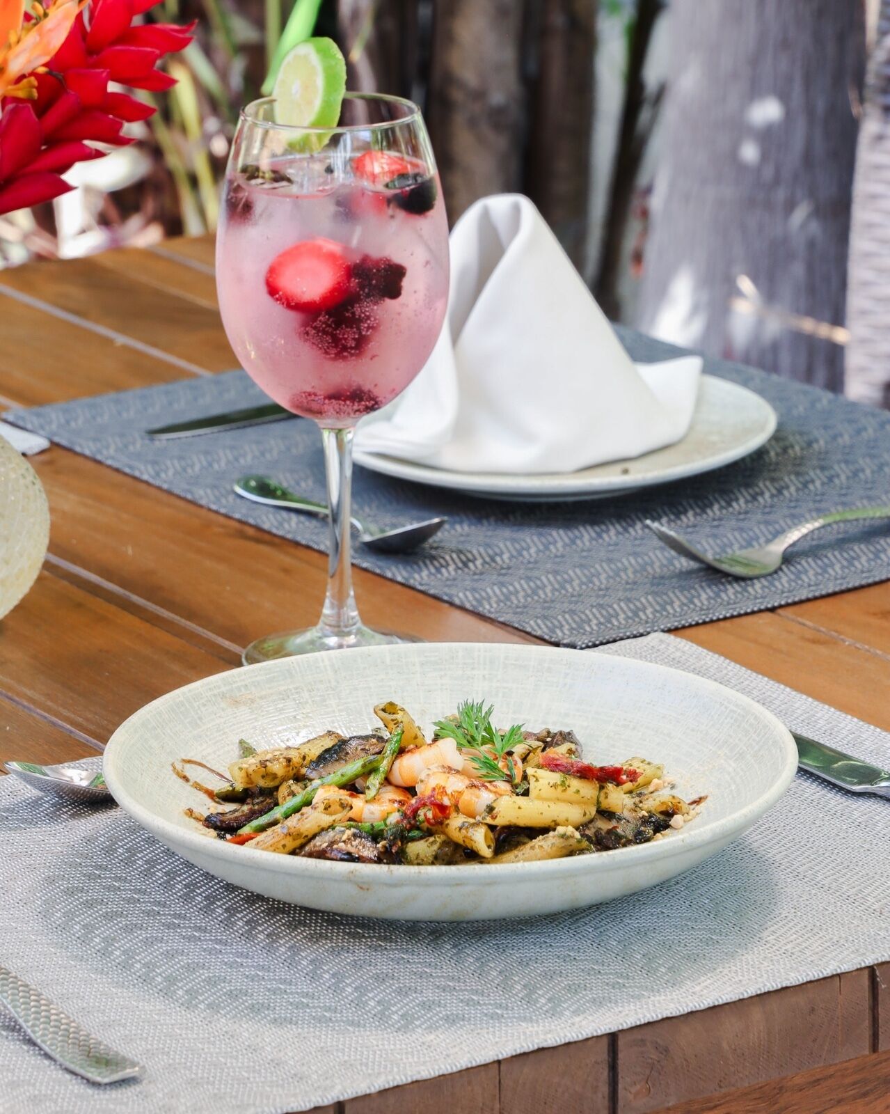 A table setting with a glass of pink beverage, a white napkin, and a plate of food.