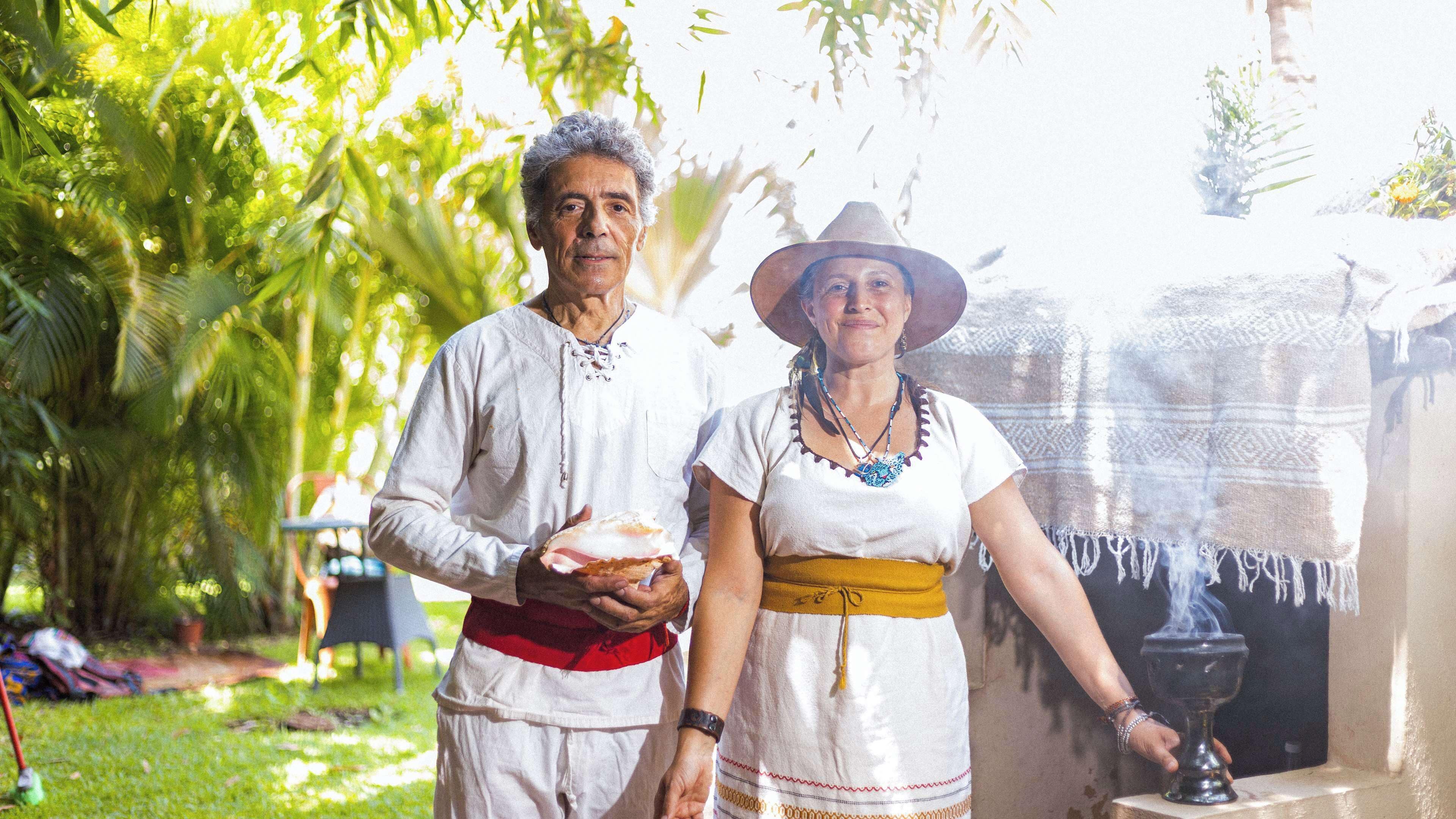 A couple dressed in traditional attire standing in a garden with a fountain.