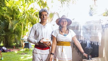 Una pareja vestida con traje tradicional posando en un jardín con una fuente.