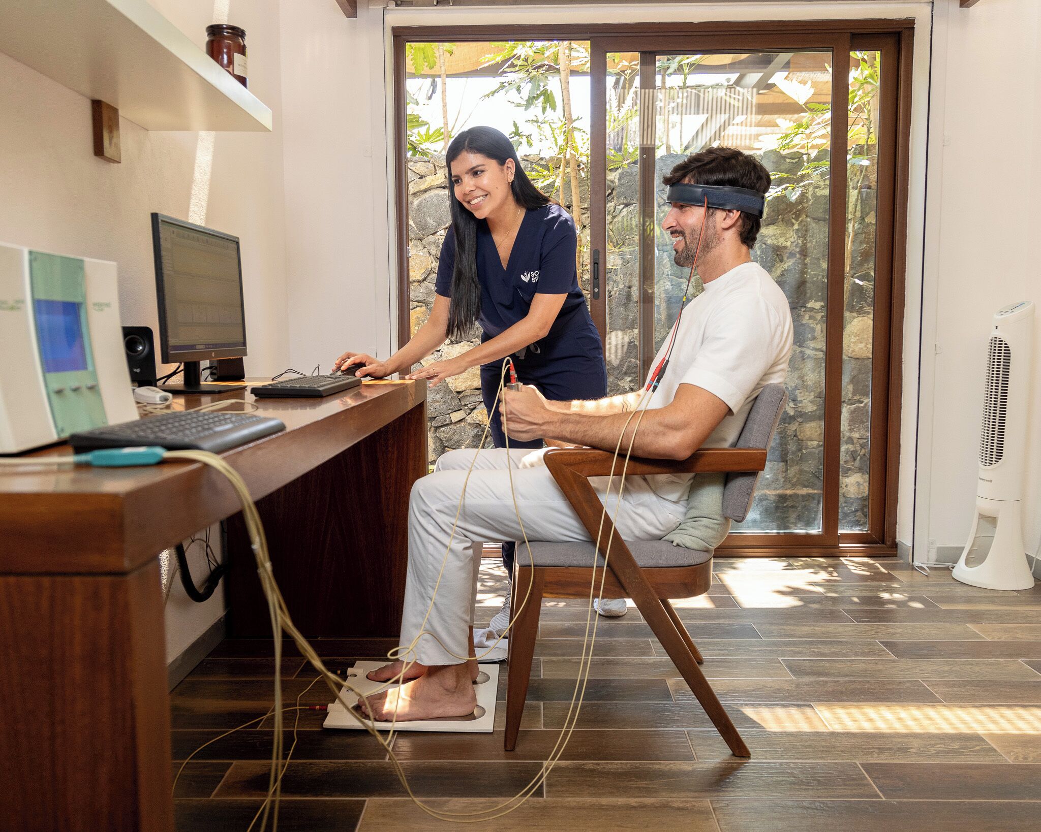A medical examination room with a patient on a scale, a computer, and a nurse.