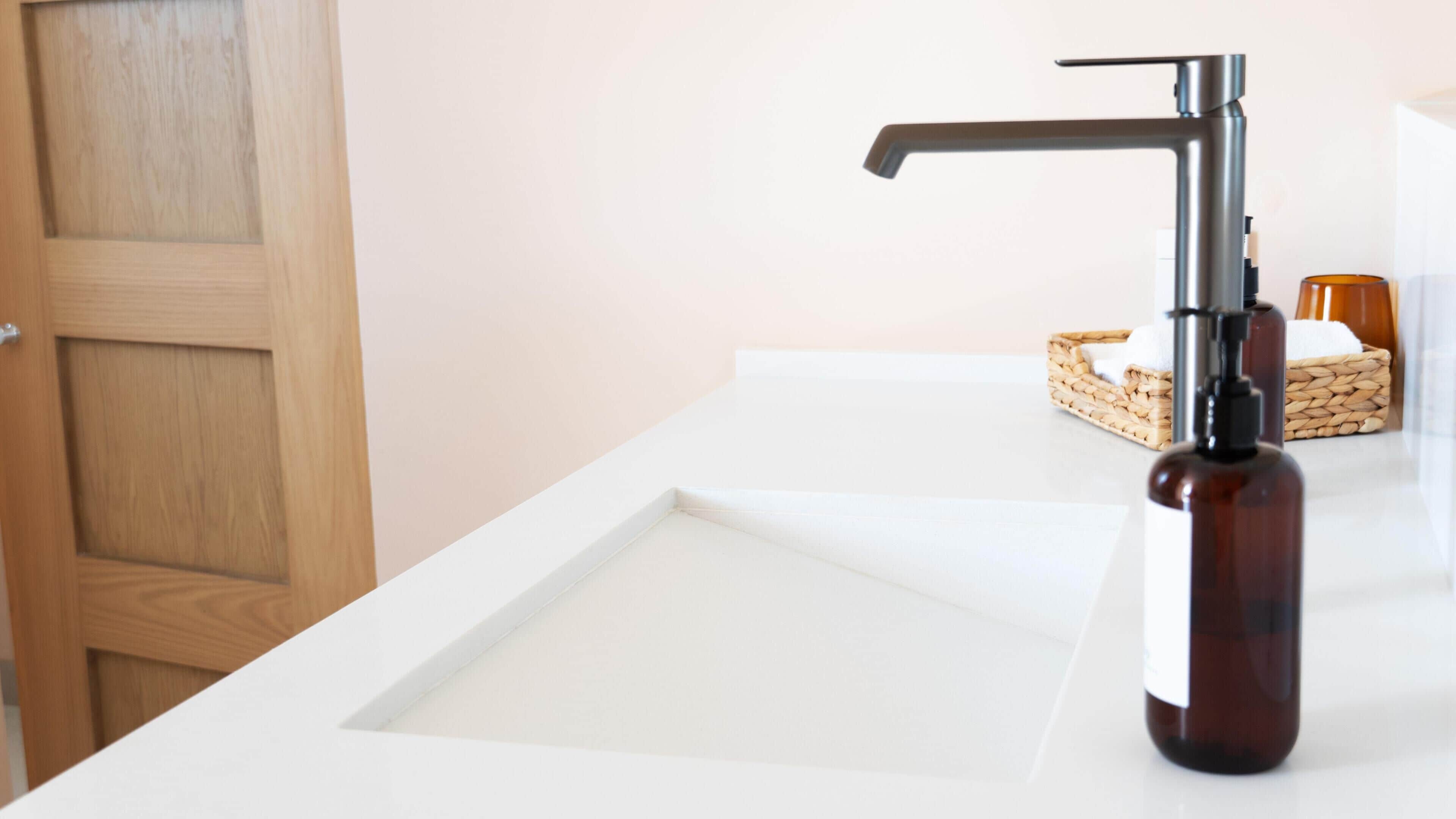A bathroom with a white sink, a wooden door, and a bottle of soap.