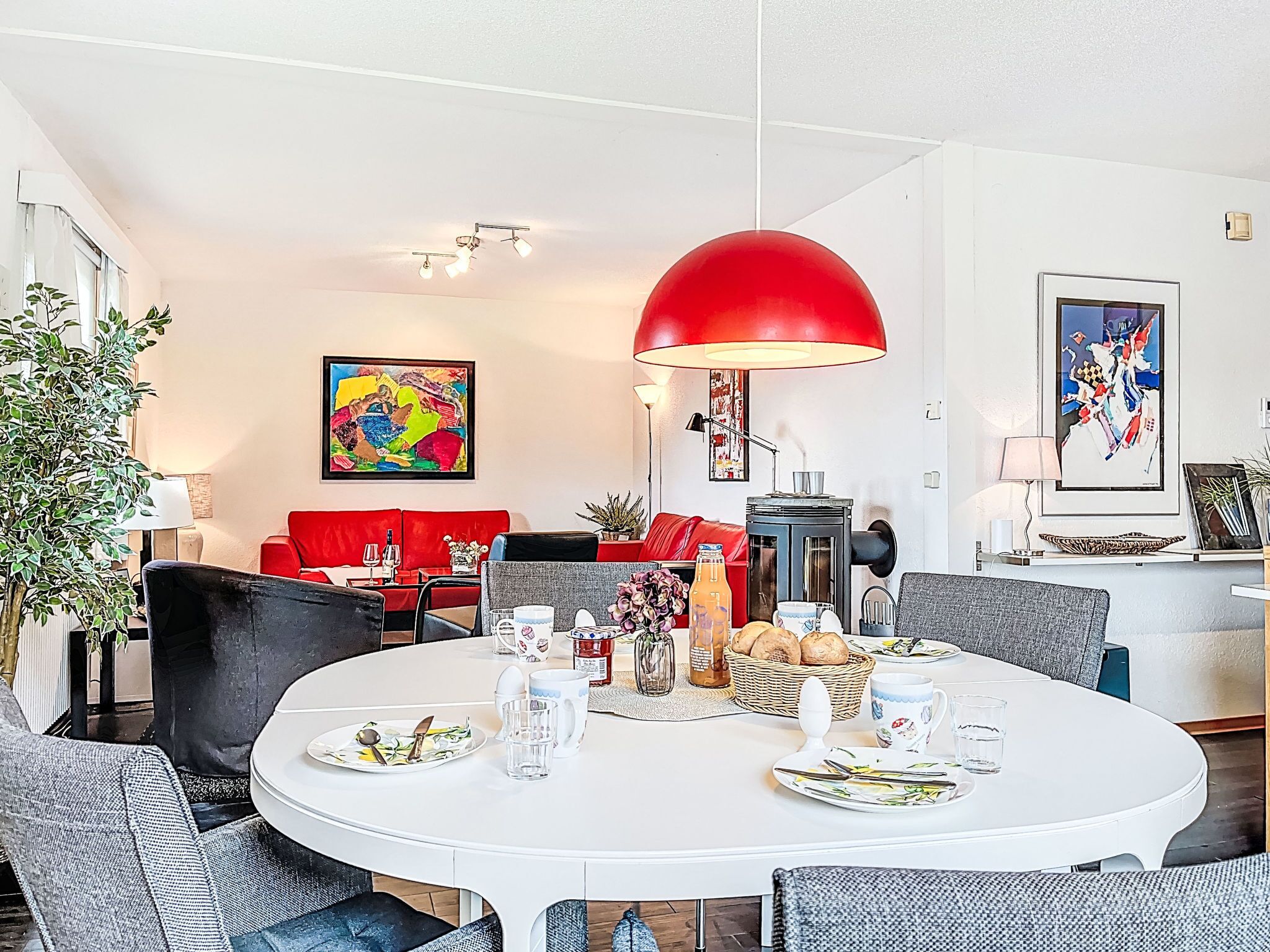 Een moderne woonkamer met een rode bank, een eettafel gedekt voor twee personen en een grote rode hanglamp.