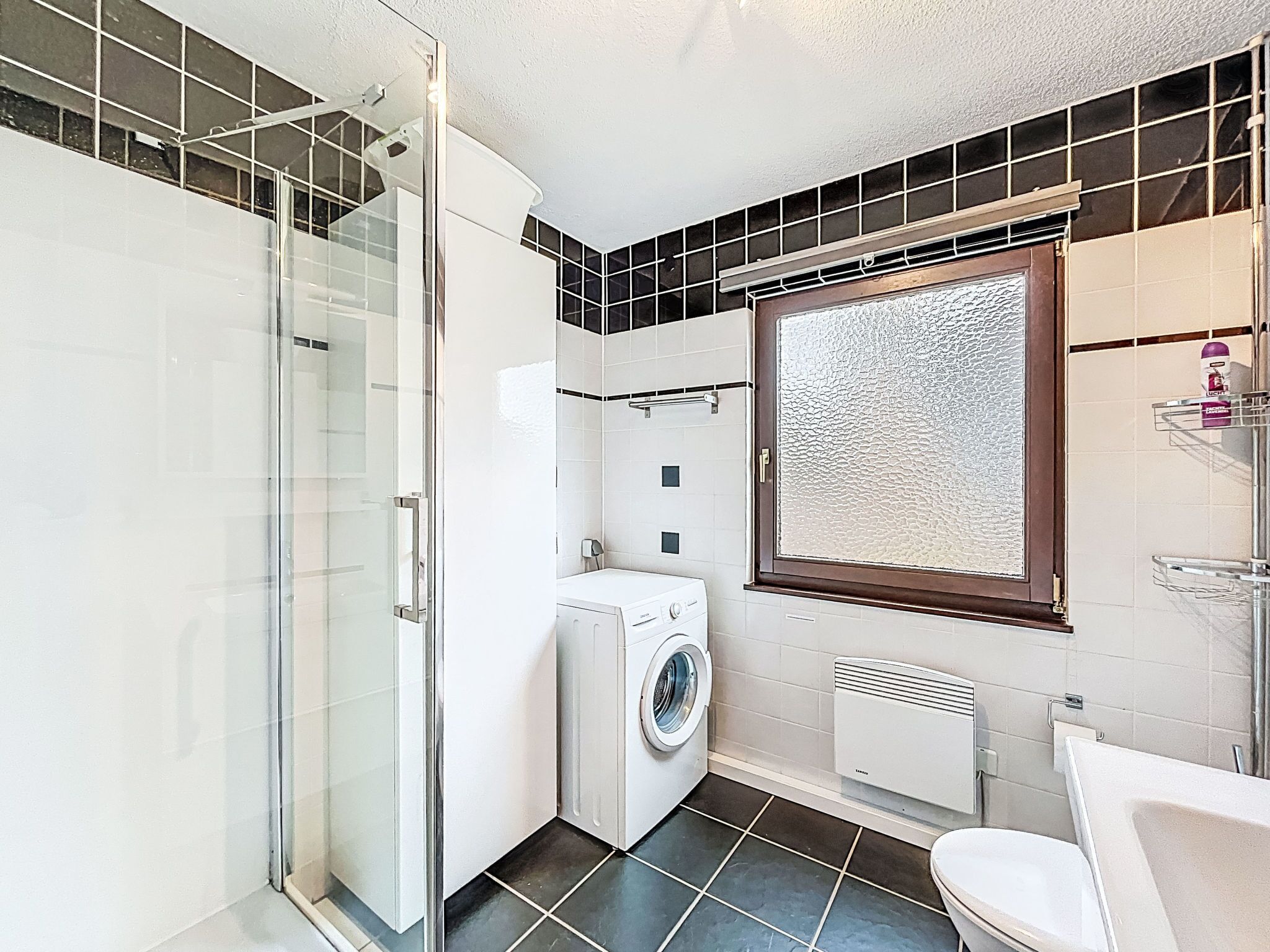 A compact bathroom with a glass shower enclosure, a washing machine, and a toilet.