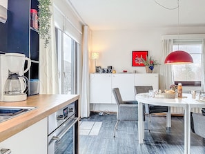Une cuisine moderne équipée d’une machine à café, d’une table à manger, de chaises et d’un luminaire suspendu rouge.