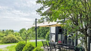 Un patio con tavolo e sedie, un pergolato e vista su una casa e il paesaggio.