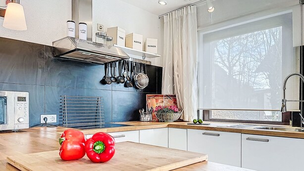 Una cucina moderna con un piano di lavoro in legno, un tagliere con peperoni rossi, un forno a microonde e una finestra con tende.