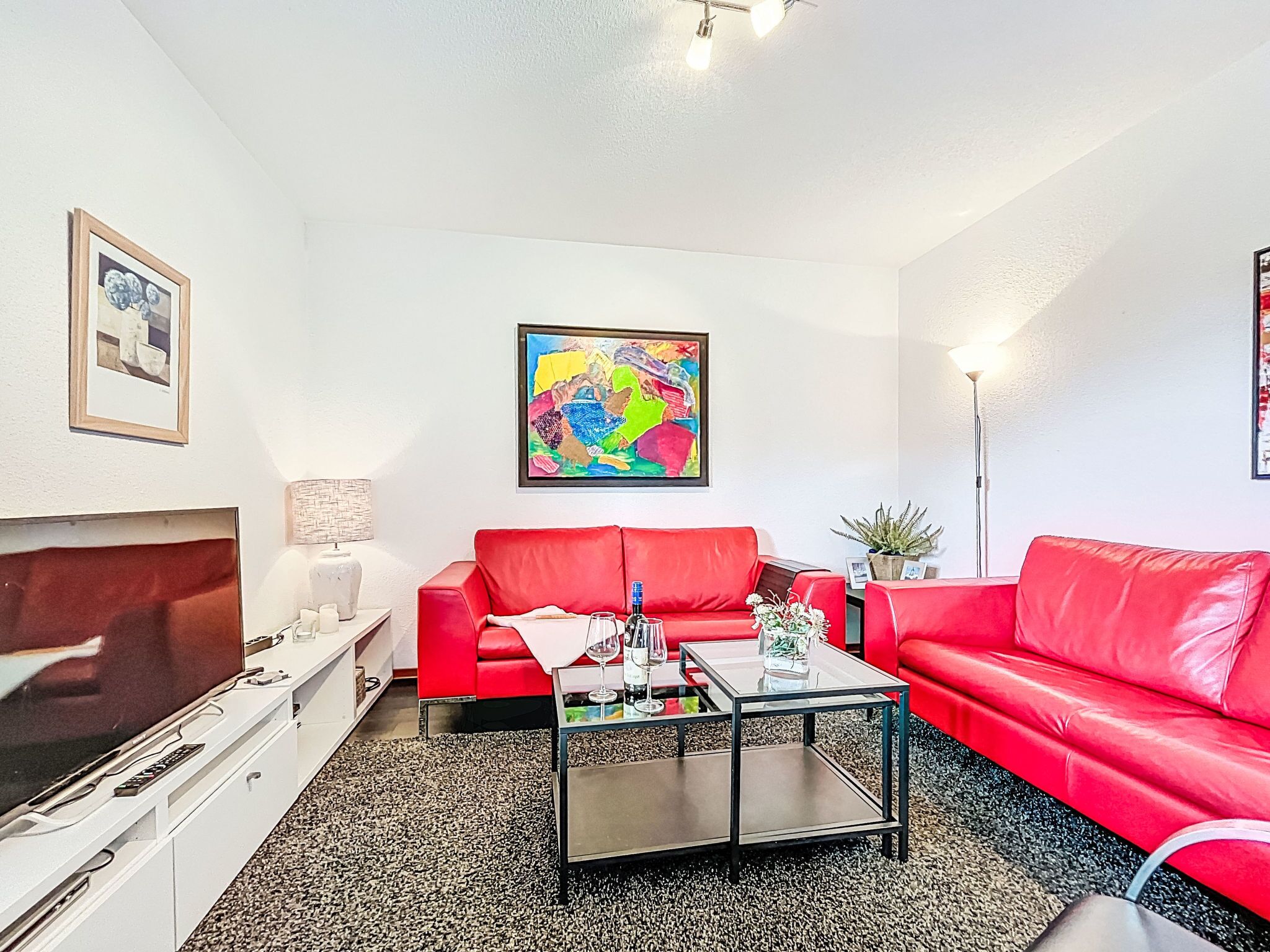 A modern living room with a red sofa, a glass coffee table, and a flat-screen TV.