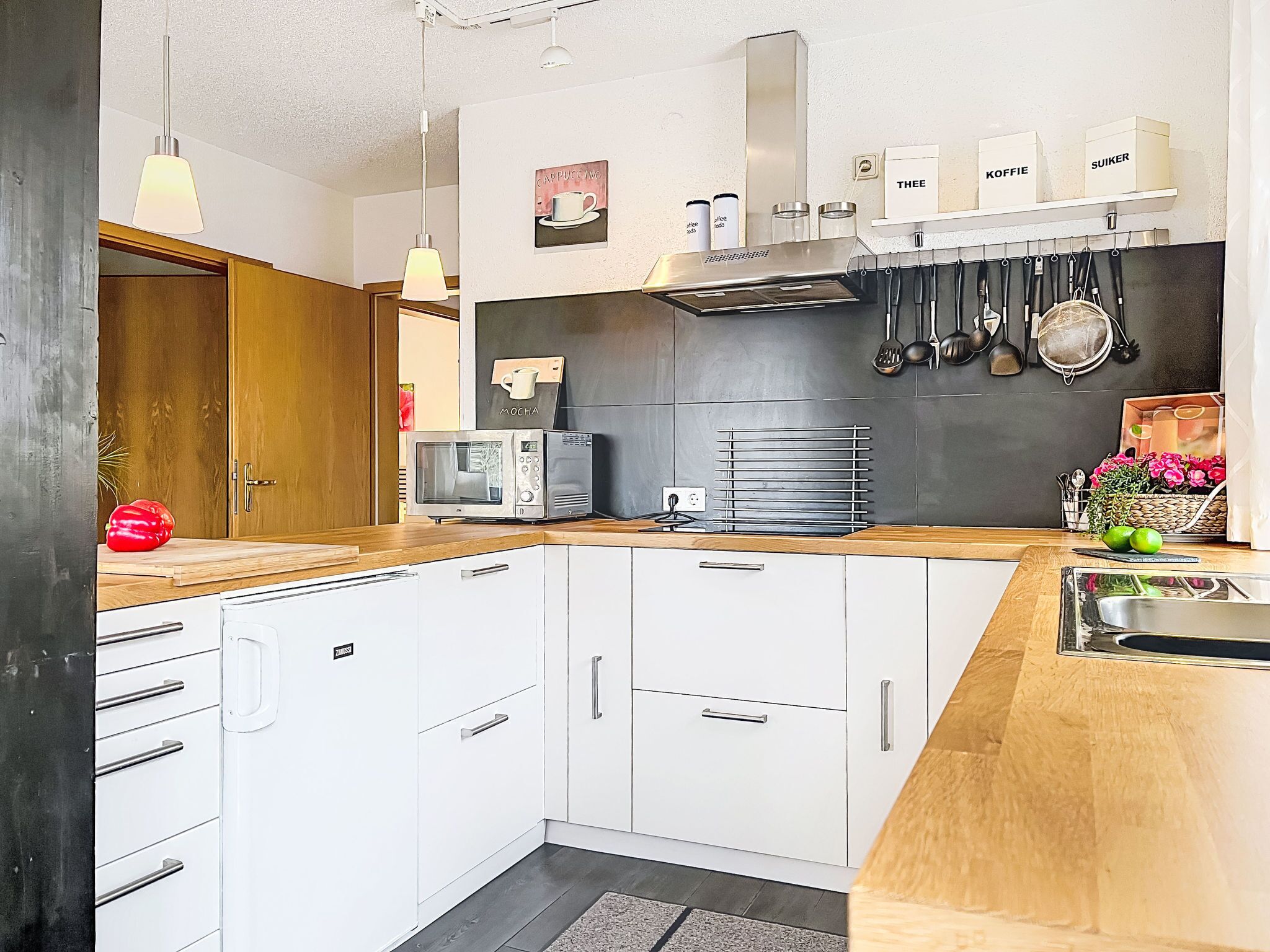 Una cocina moderna con armarios blancos, un microondas, una cafetera y varios utensilios de cocina en la pared.