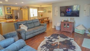 A modern kitchen with a refrigerator, microwave, and cabinets. There is a dining area with a table and chairs. A gray sofa and a cowhide rug are in the living room. A flat-screen TV is mounted on the wall. - Pet friendly w/dog run, country living & mountain views close to town with wifi (Springfield)