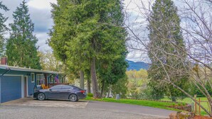 A residential house with a car parked in the driveway, surrounded by trees and a grassy yard. - Pet friendly w/dog run, country living & mountain views close to town with wifi (Springfield)