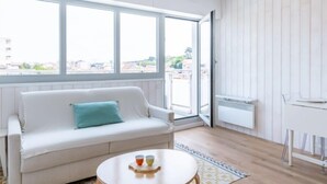 Ein modernes Wohnzimmer mit einem weißen Sofa, einem runden Couchtisch und einem großen Fenster mit Blick auf die Stadt.