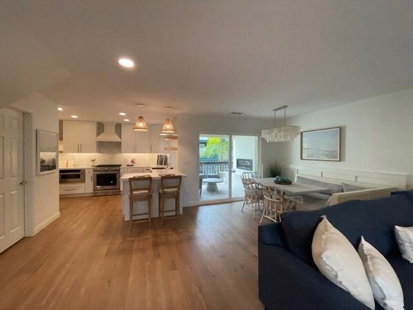 A spacious living area with a dark blue sofa, a dining table with chairs, and a kitchen area with modern appliances and pendant lighting.