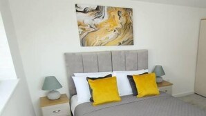 A bedroom with a grey bed, two nightstands, a radiator, and a painting on the wall.