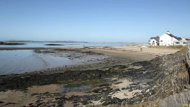 A coastal area with a rocky shoreline, a sandy beach, and a white building with a dark roof.