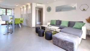 Un salon moderne avec un canapé gris, des coussins verts, une table basse blanche et un coin repas avec des chaises vertes.