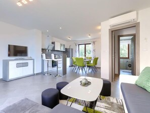 Un salon moderne comprenant un canapé, une table à manger avec des chaises, un coin cuisine et un téléviseur fixé au mur.